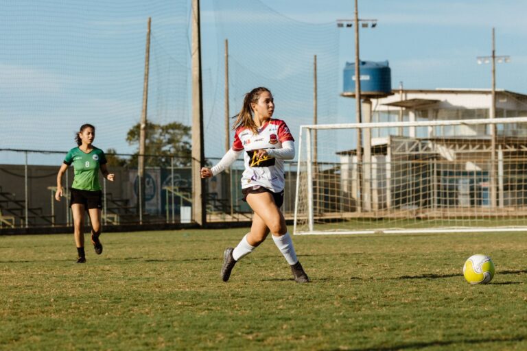 Two women soccer players in action on a grassy field under sunny conditions.