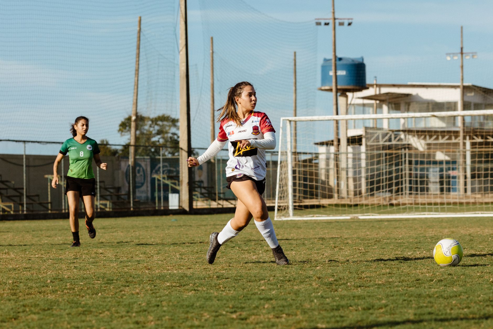 Two women soccer players in action on a grassy field under sunny conditions.