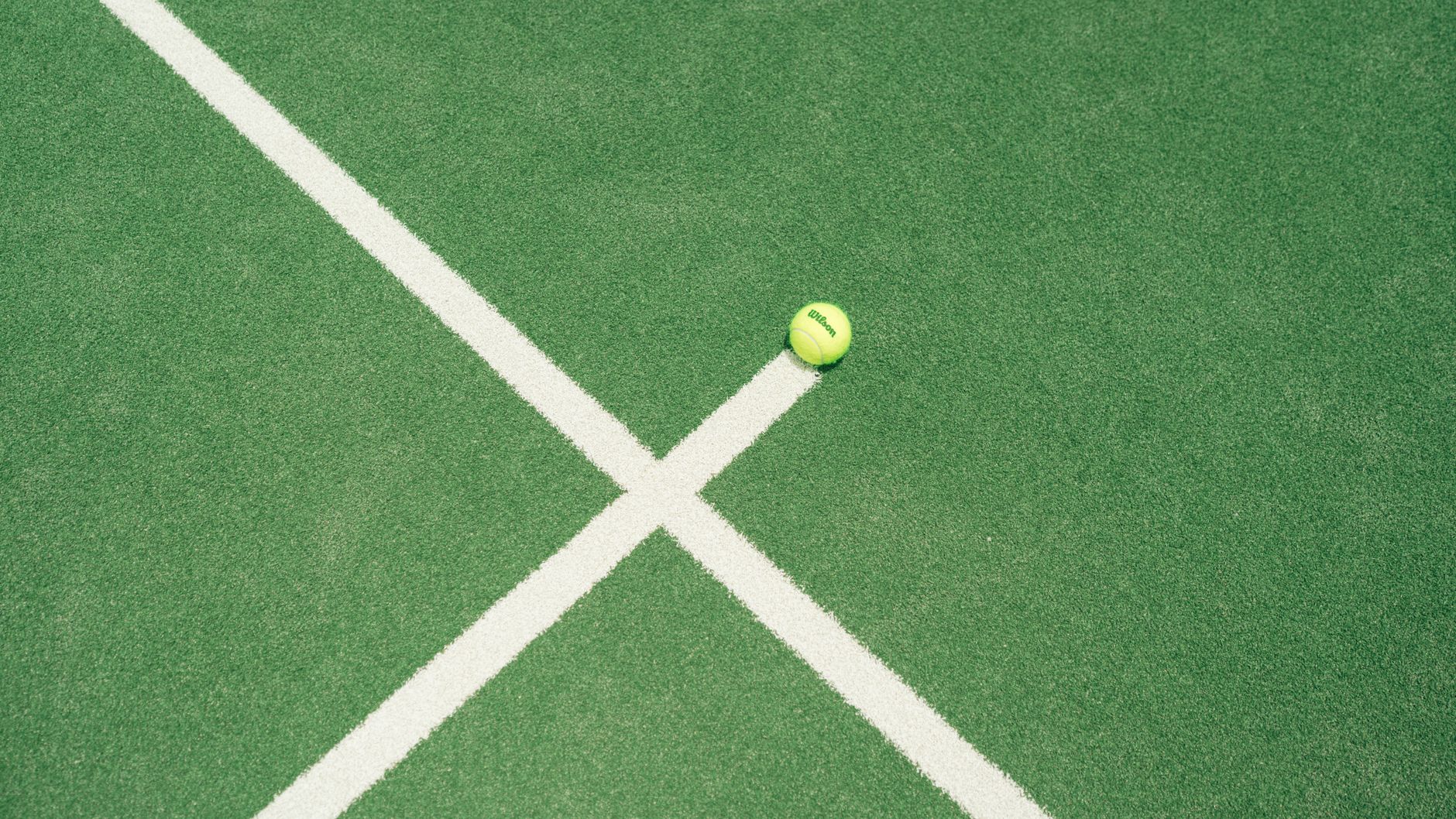 A bright green tennis ball on a green tennis court with white lines in Miami, FL.
