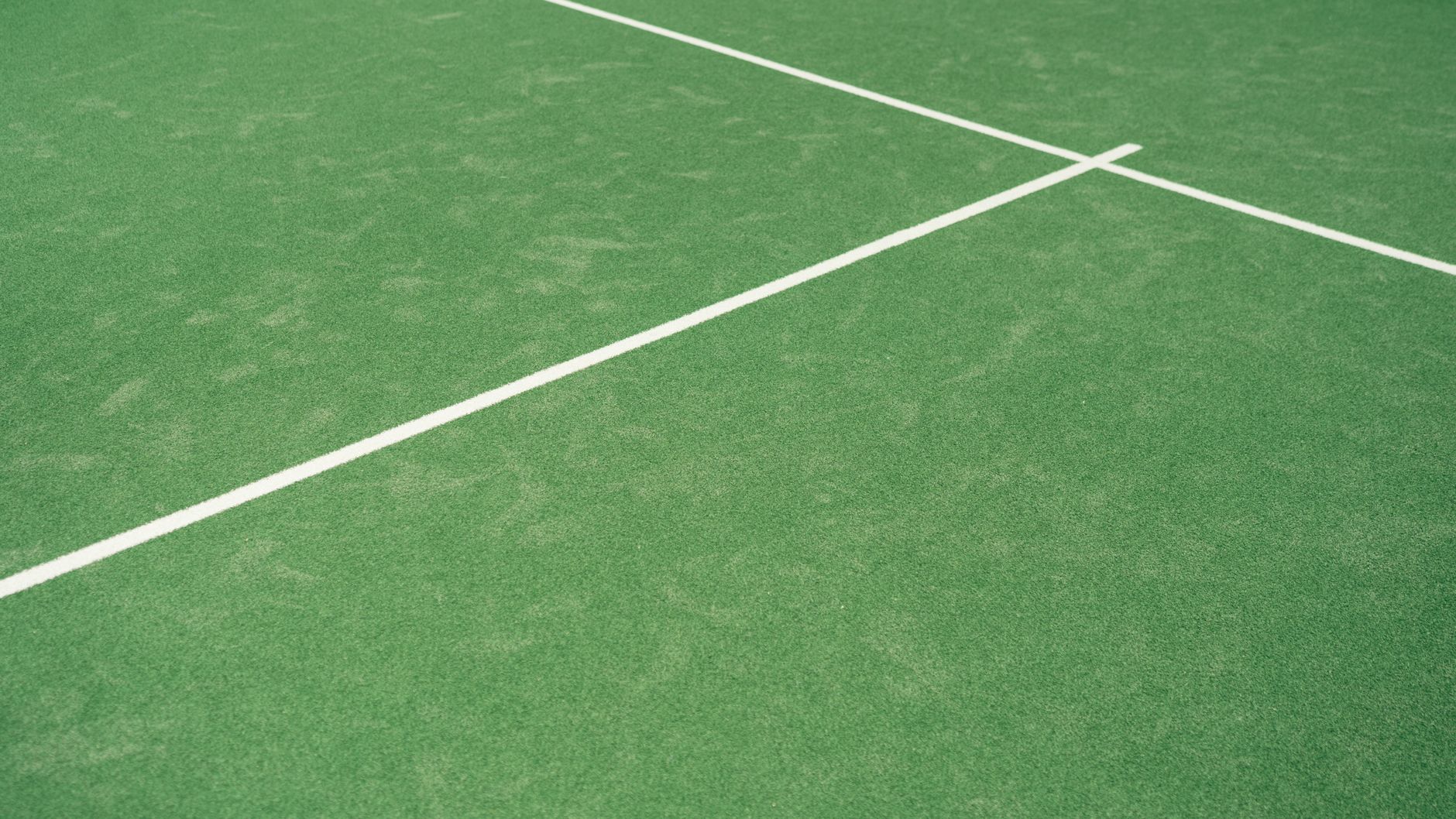 Close-up view of tennis court's vibrant green surface with white lines