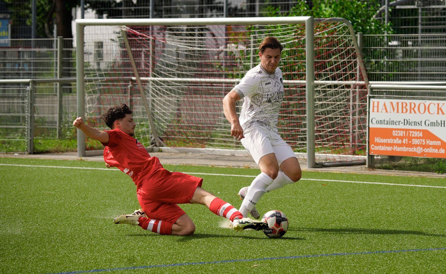 Two footballers in a dynamic sliding tackle on a sunny day during an exciting soccer match.