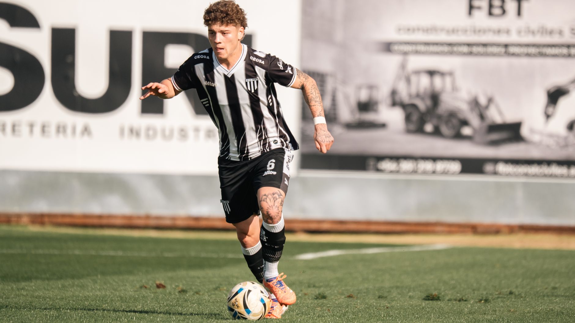 A soccer player in black and white uniform dribbling the ball during a day match.