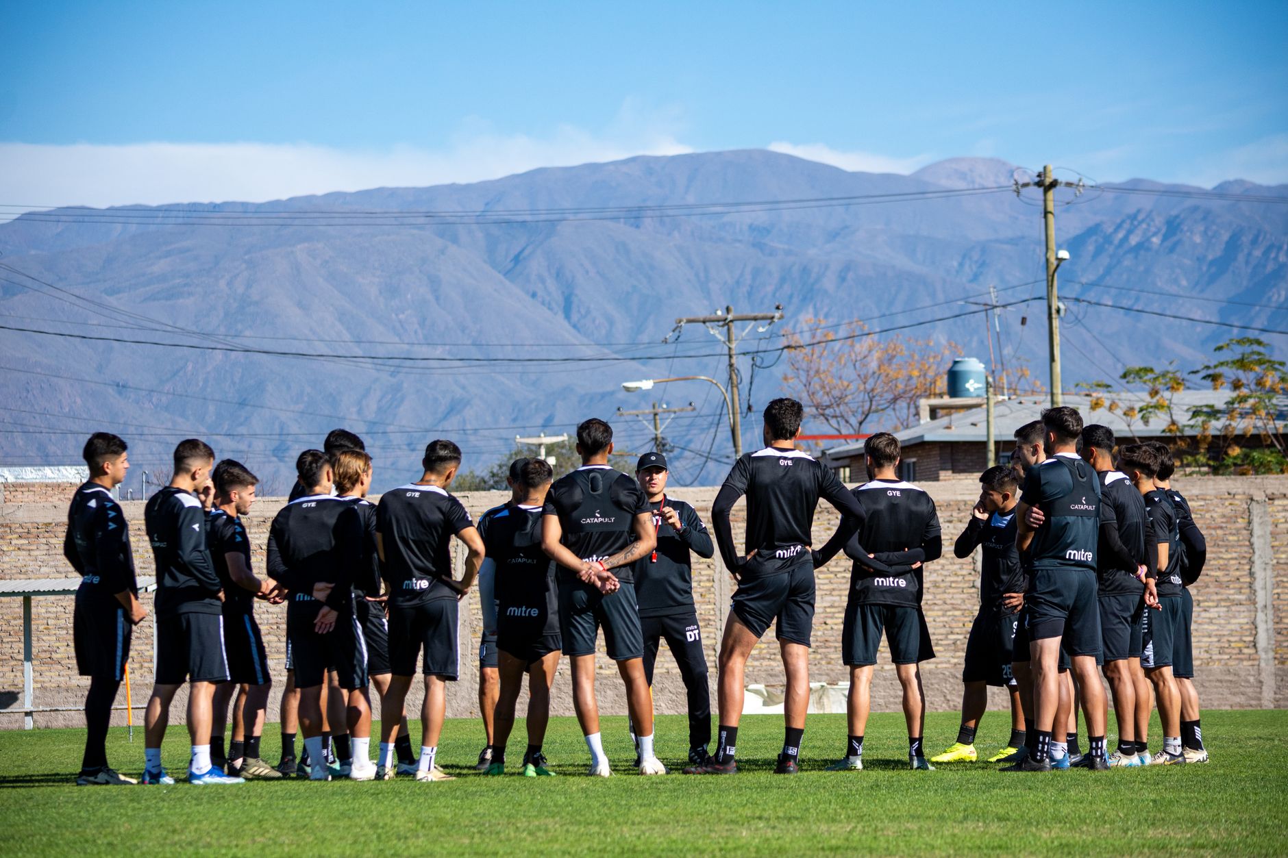 A group of footballers training outdoors with mountains in the background.