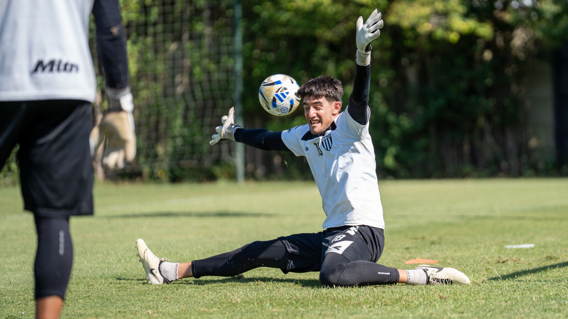 Soccer goalkeeper intensely focused while making a save during practice on a sunny day.