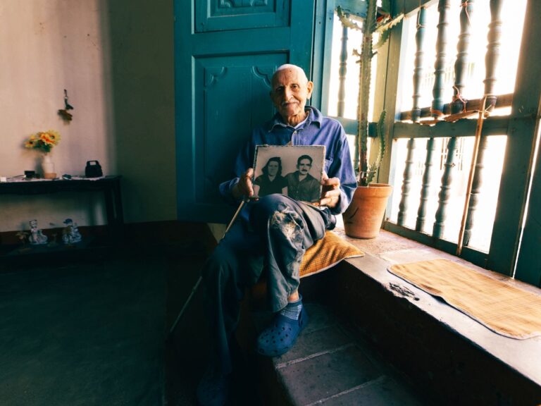 Senior man seated by window, reminiscing with a nostalgic photo.