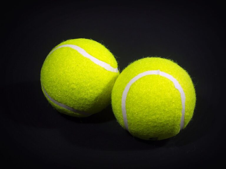 Two bright yellow tennis balls on a dark background with visible texture and shadows.
