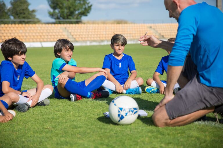 Boys listen intently to their soccer coach on a sunny soccer field.