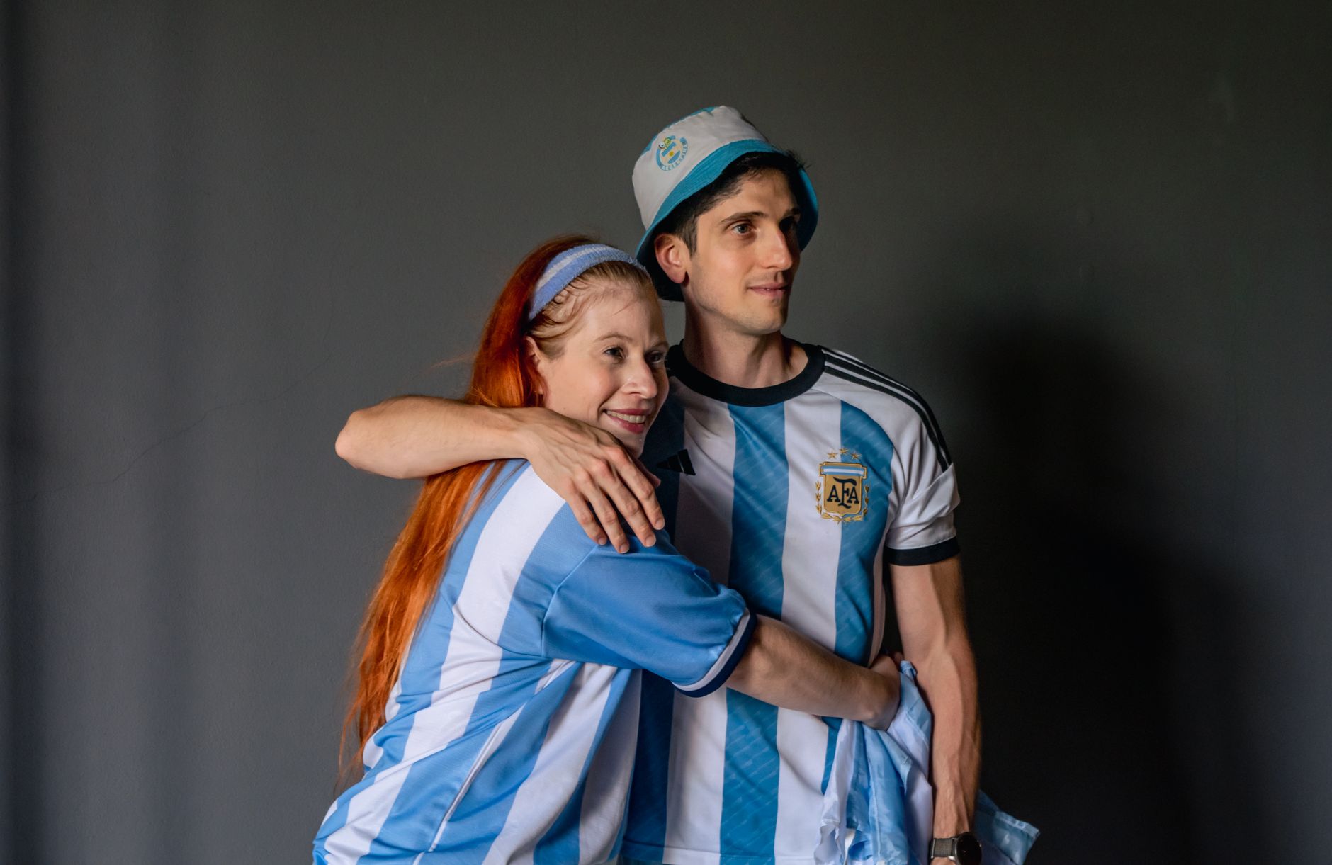 A couple in Argentina jerseys embraces, celebrating a soccer game.