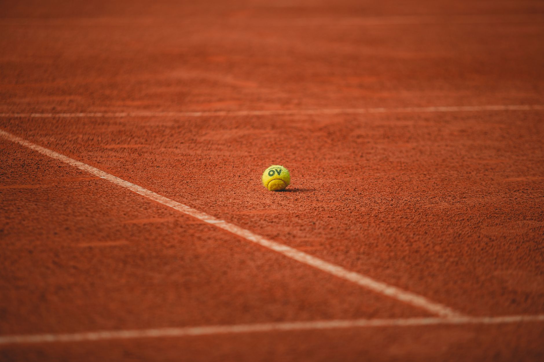 A lone tennis ball rests on a red clay tennis court, highlighting its vibrant texture.