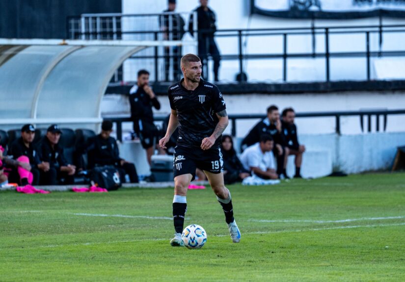 Soccer player dribbling during a match with team watching from the sidelines.