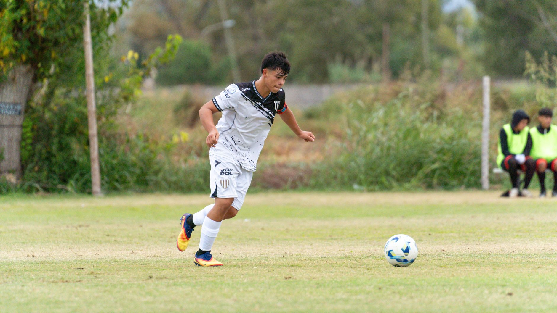 Teen soccer player dribbles the ball on the field during a competitive match.