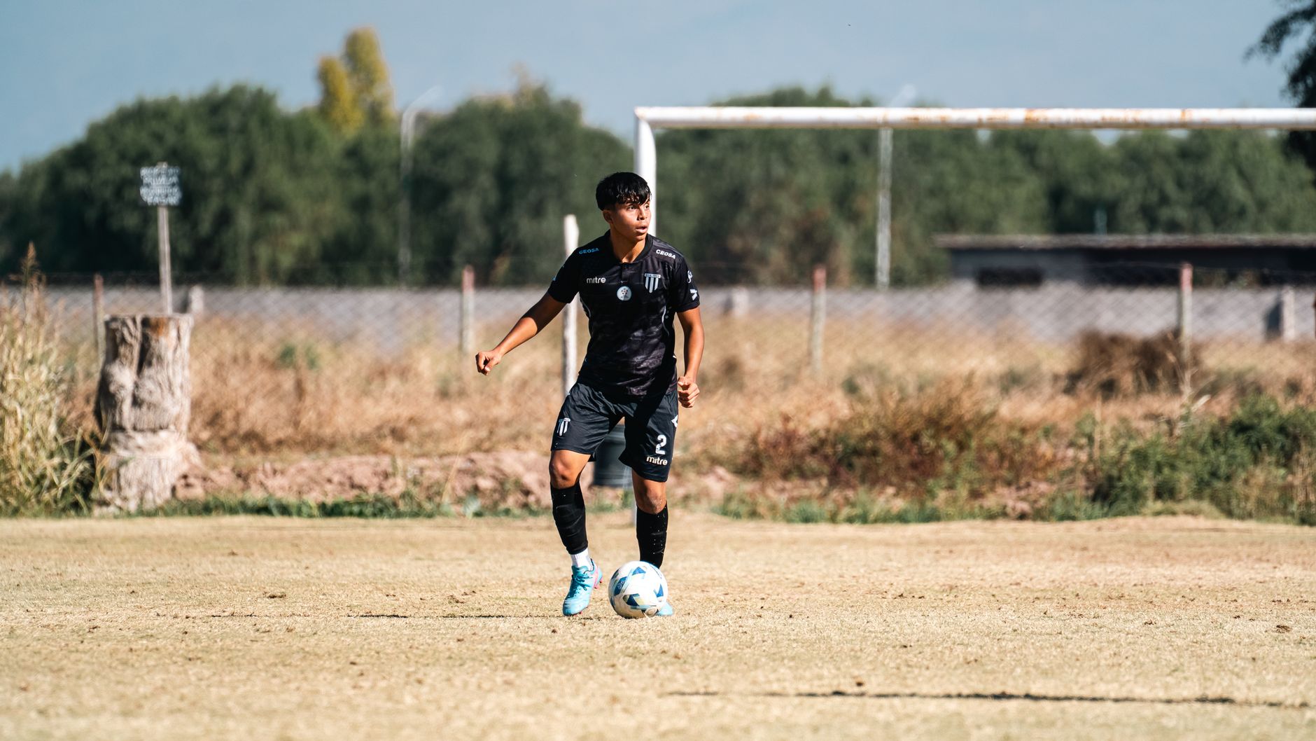 Teen soccer player in uniform on a sunny day, ready to kick the ball outdoors.