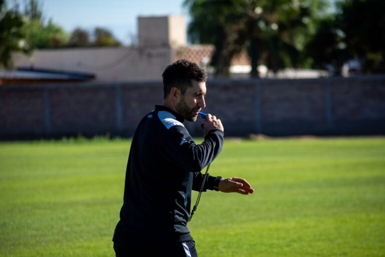 Football coach blowing a whistle during practice on a sunny day outdoors.