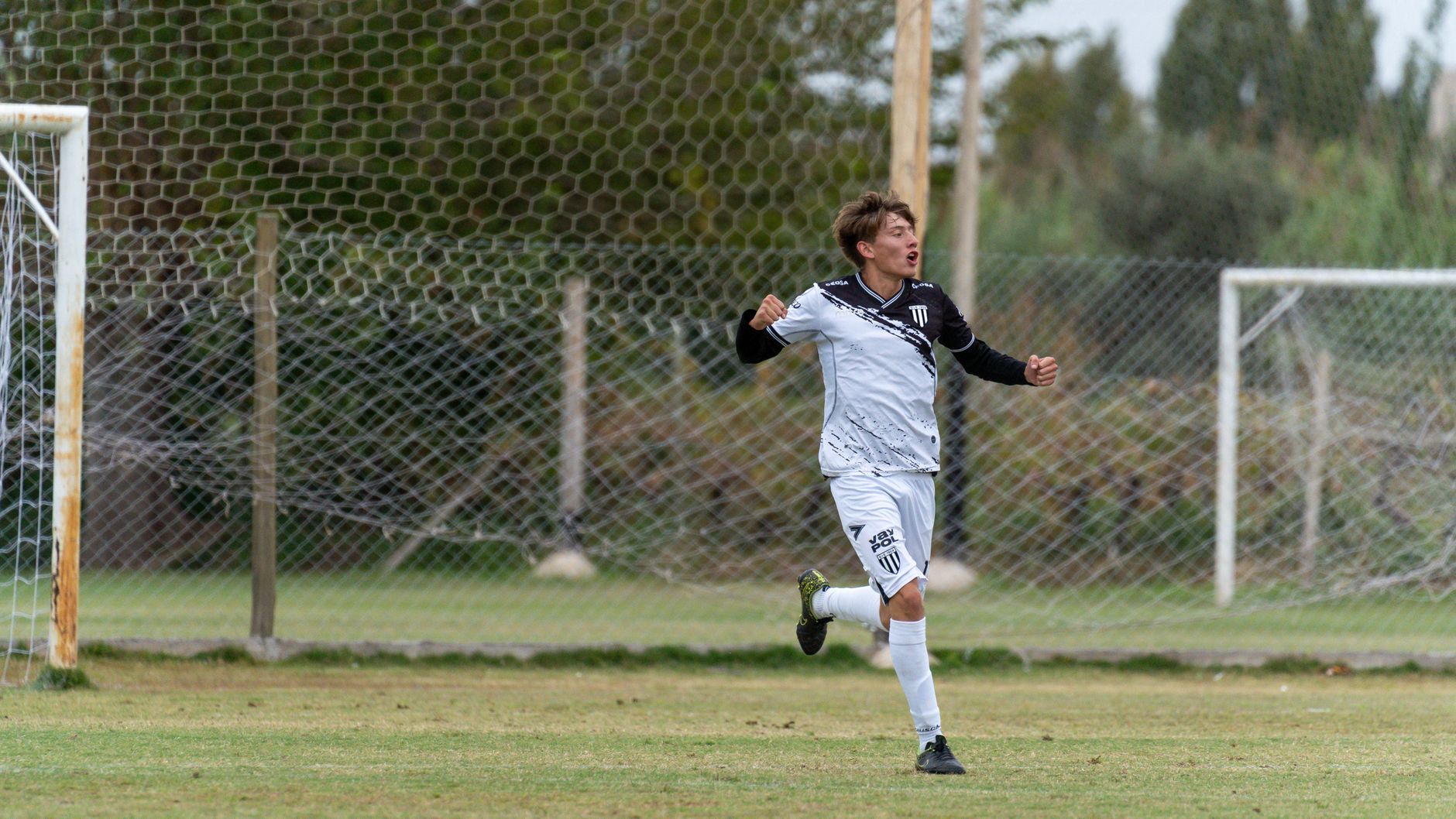 A young soccer player joyfully celebrates scoring a goal on an outdoor field.