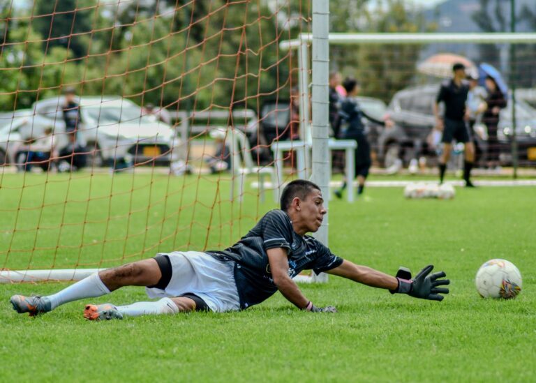 Goalkeeper diving towards the ball on a soccer field during a match.