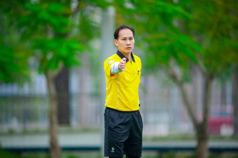 Referee signaling during a soccer match in Hanoi, Vietnam, on a green field.