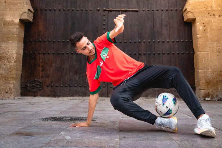 A young man skillfully performs a soccer trick with a ball, showcasing talent and athleticism in a vibrant urban setting.