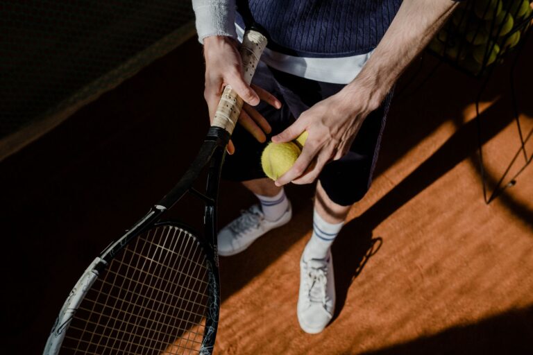 A tennis player prepares for a serve, holding a racket and tennis ball on a clay court.
