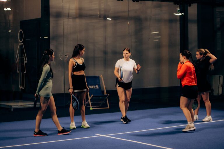 Group of women playing paddle tennis indoors, discussing strategies in an evening match.