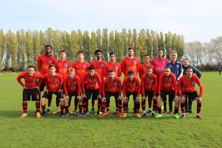 A local soccer team posing on a sunny day on the field.