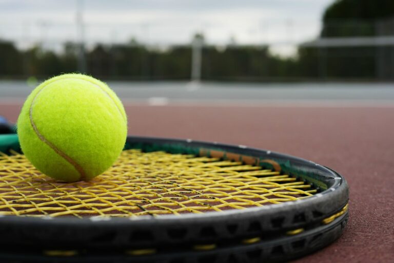Vibrant tennis ball resting on a racket against a blurred court background.