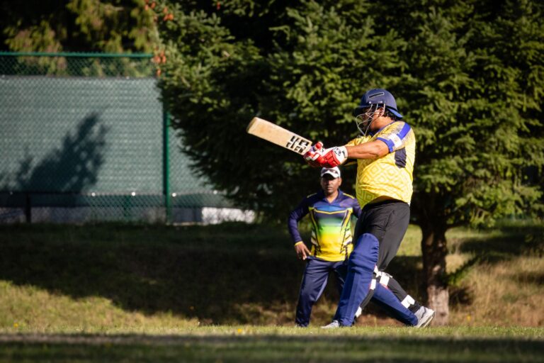 Action shot of a cricketer batting during an outdoor match on a sunny day.