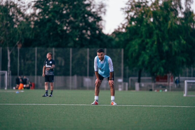 Male soccer player in uniform standing in field and leaning on hands during training in grassy field
