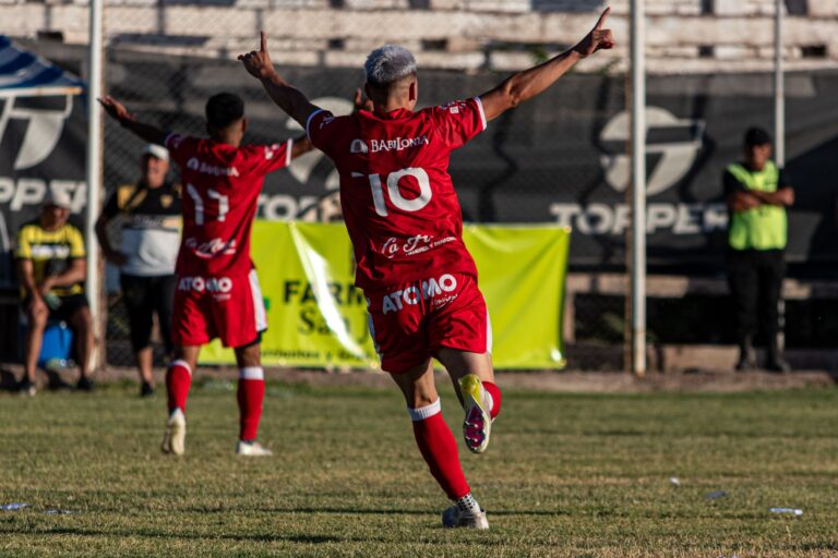 Soccer players in red jerseys celebrate a goal during a match under a sunny day.