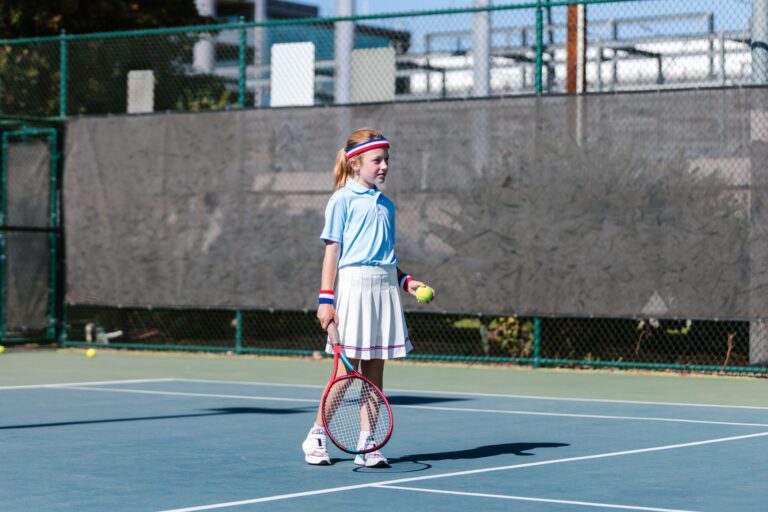 A young girl in sportswear playing tennis on an outdoor court. Bright, sunny day.