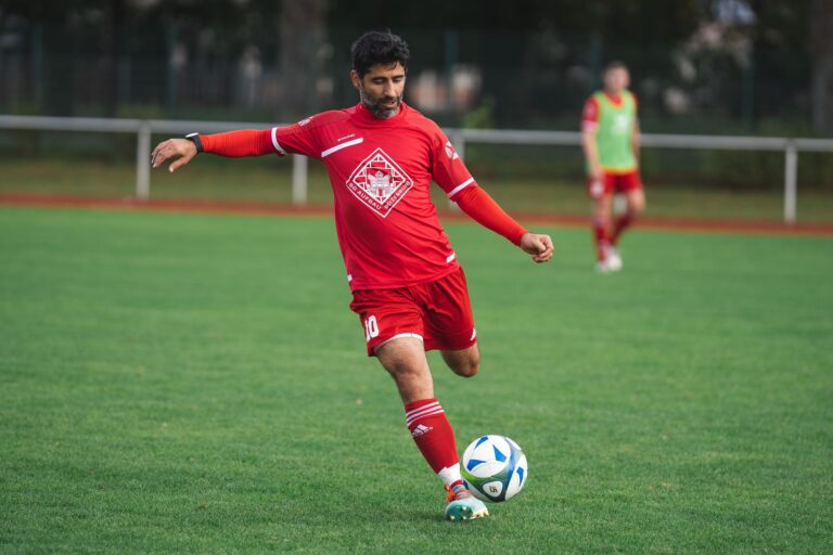 Soccer player in red uniform kicks ball on a green field. Action shot outdoors.