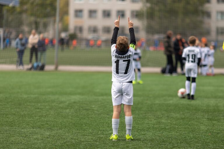 A young soccer player raises hands in celebration on an outdoor field.