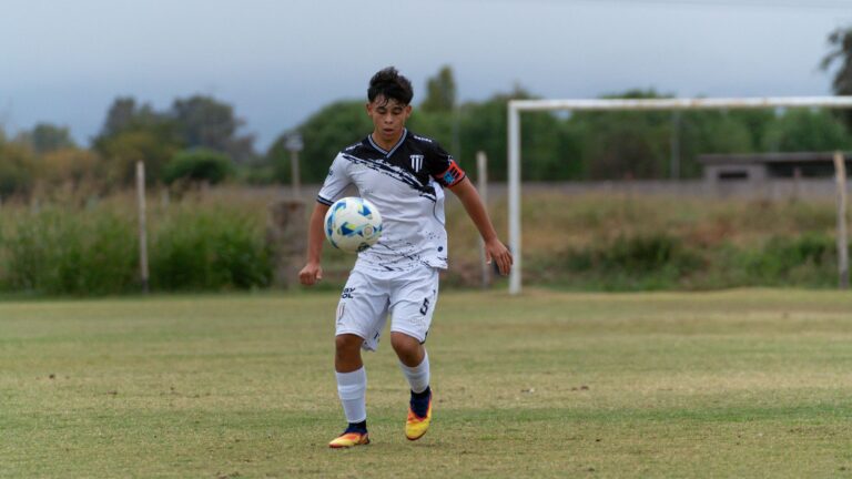 A teenage soccer player focuses on controlling the ball during a match on a grassy field.