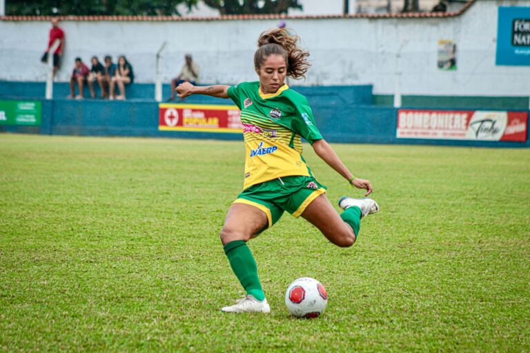 Dynamic action shot of a female soccer player kicking a ball on the field during a match.