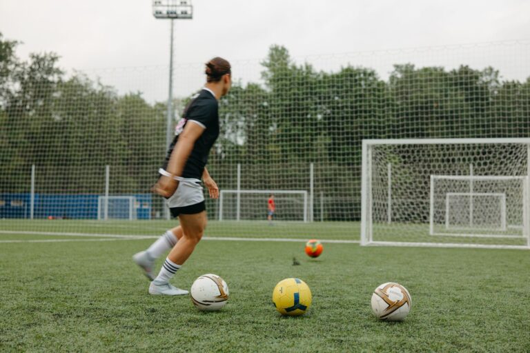 A woman practicing soccer on an outdoor field with multiple soccer balls and goals.