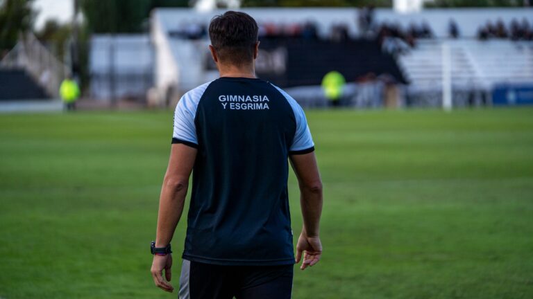 Back view of soccer coach at Gimnasia y Esgrima stadium during a match.