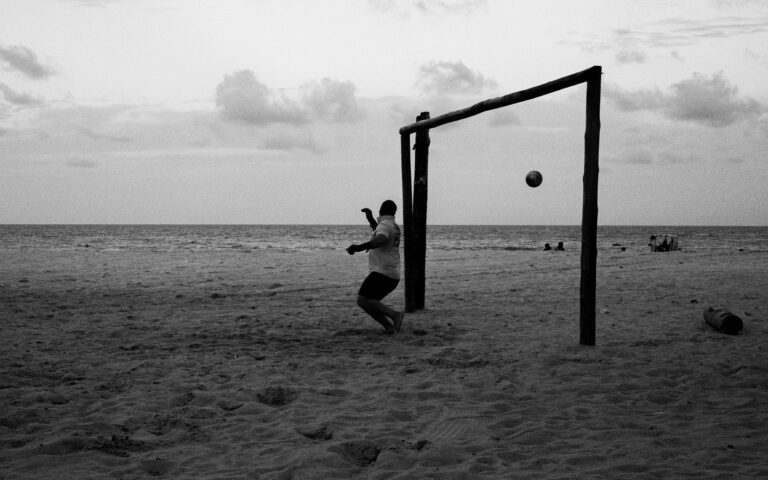 A monochrome shot of a soccer game on a beach in Natal, Brazil during twilight.