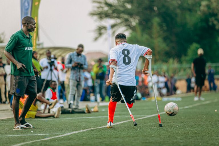 Amputee athlete playing soccer with crutches, showing determination and inclusivity.