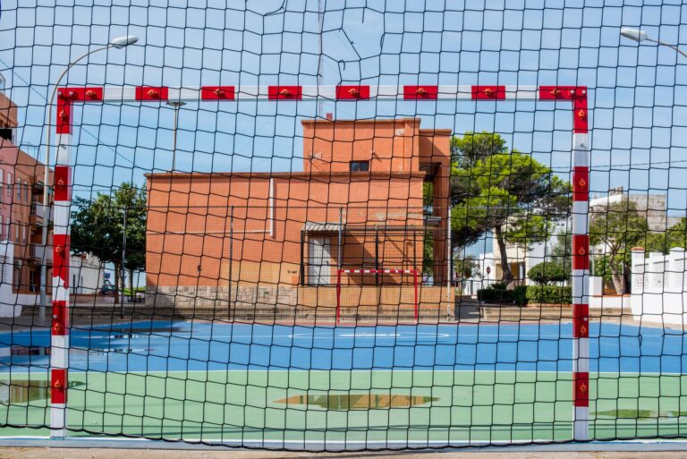 A vibrant sports field with a goal net under clear skies in El Perellonet, Spain.