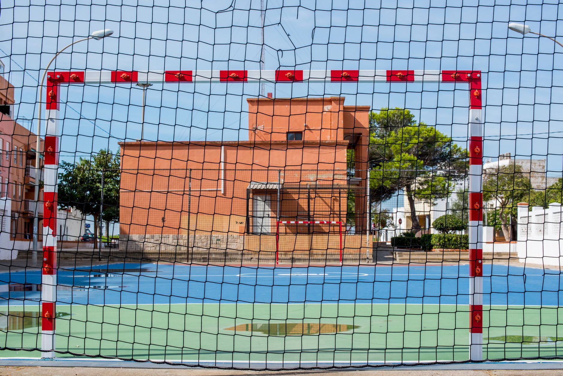 A vibrant sports field with a goal net under clear skies in El Perellonet, Spain.