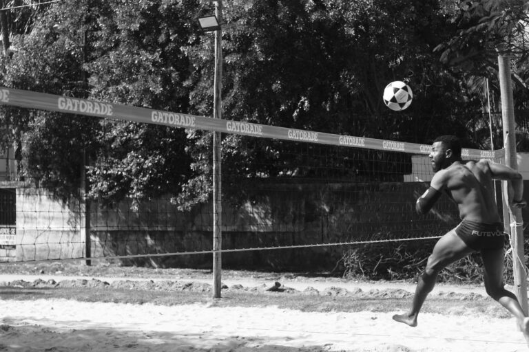 Black and white photo of a futevôlei player hitting a ball on a sandy court in Ilhéus, Brazil.