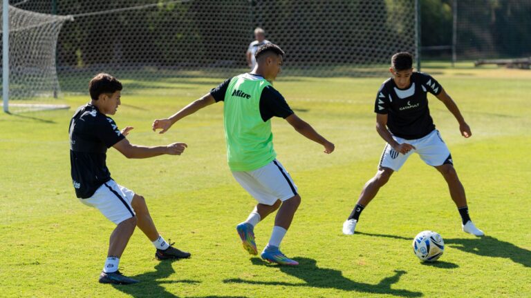 Three young men engage in soccer practice outdoors on a sunny day.