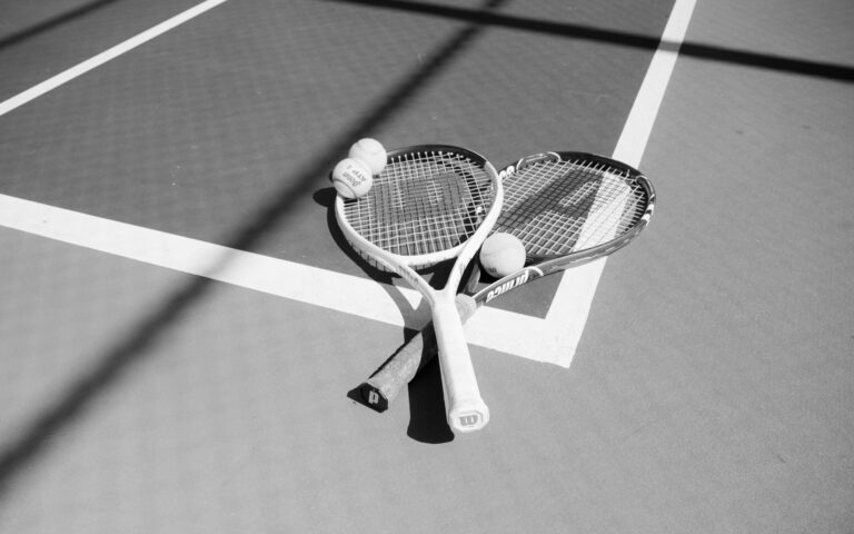 Monochrome image of two tennis rackets and balls on a sunlit court.