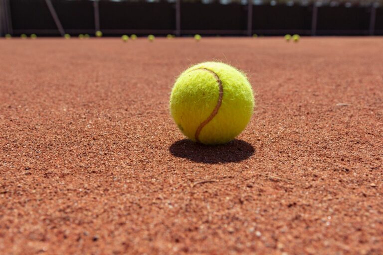 Yellow tennis ball on clay court surface, highlighting texture and sports theme.