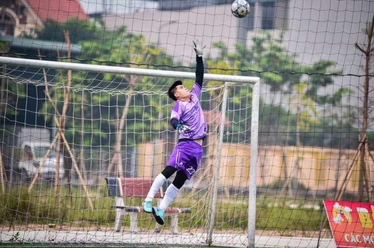 A goalkeeper makes a dynamic save during a football match in Hà Nội, Việt Nam.