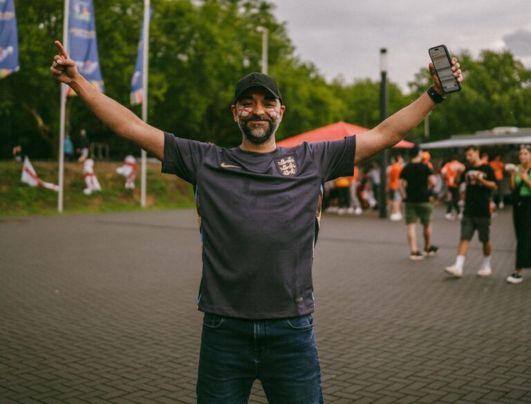 Joyful soccer fan with arms raised, celebrating outdoors in casual sportswear.
