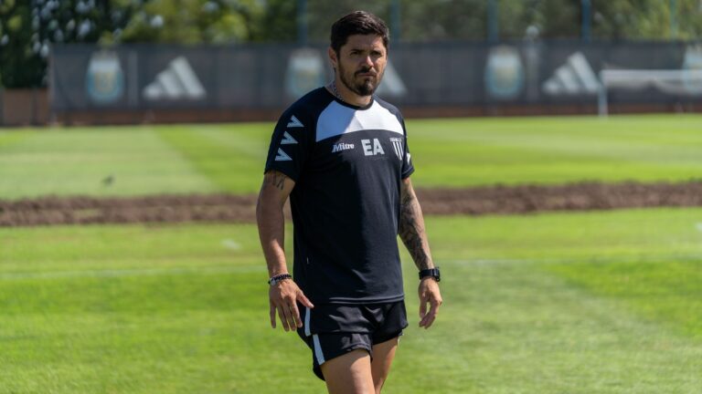 A sports coach walks confidently on a sunny training field.