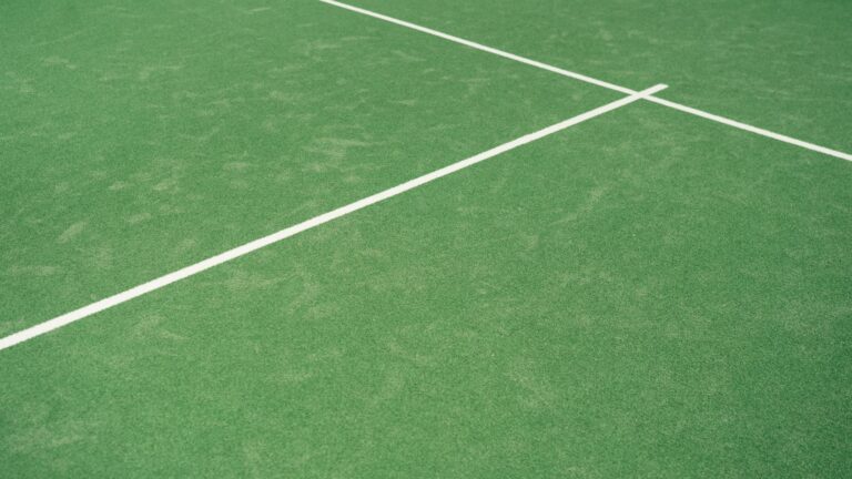 Close-up view of tennis court's vibrant green surface with white lines