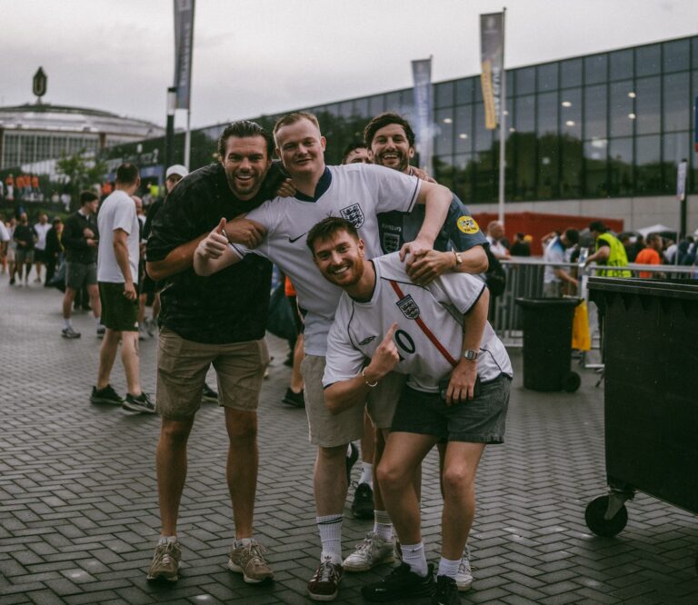 Group of enthusiastic football fans posing outside a stadium in England, showing camaraderie.