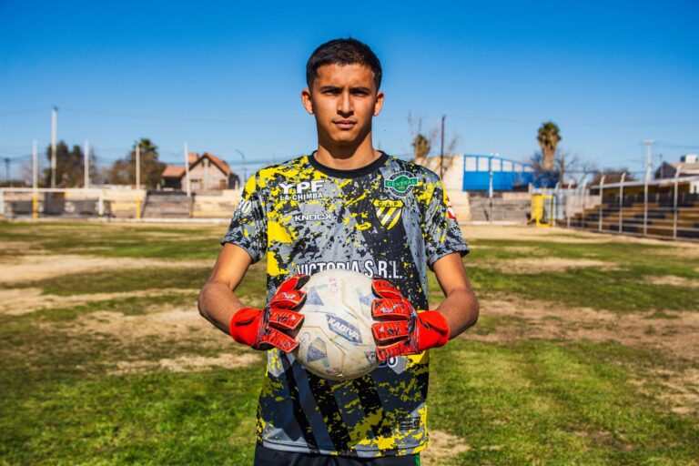 A young soccer player proudly holds a ball on a sunny day in an outdoor field.