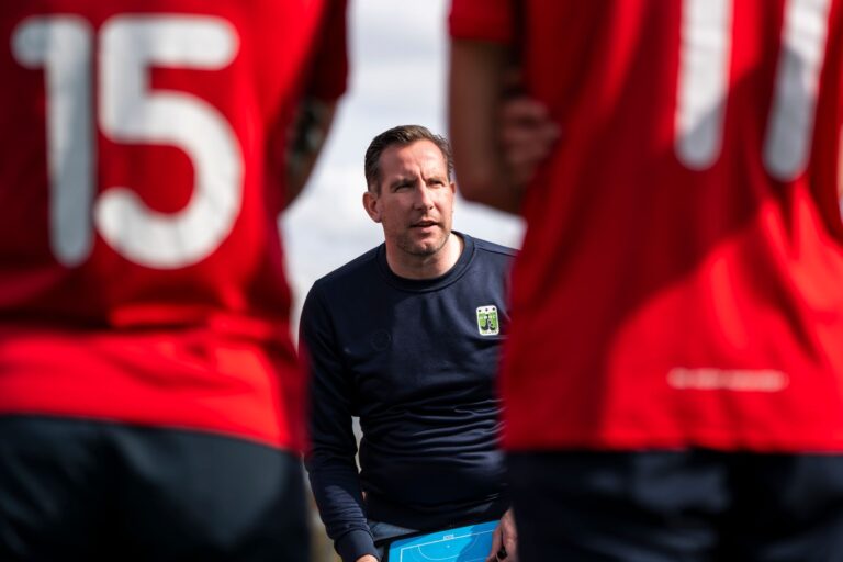 A soccer coach discusses strategy with players during daytime practice outdoors.